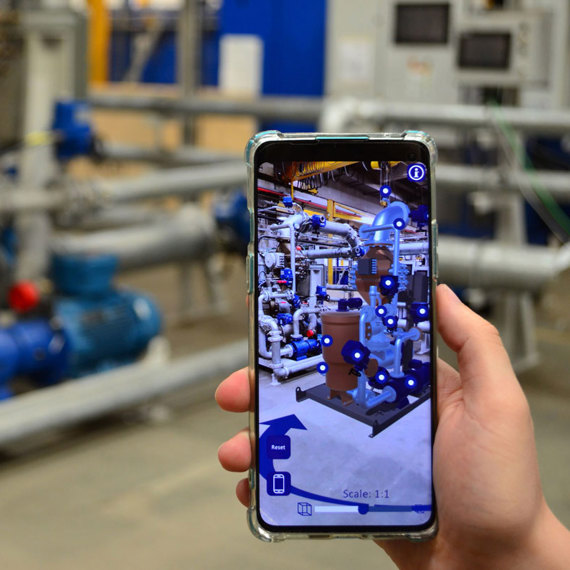 Person using augmented reality app to view industrial equipment layout on smartphone.