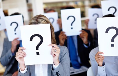 People holding papers with question marks covering their faces.