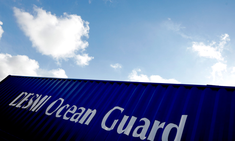 Blue container with "DESMI Ocean Guard" text under a cloudy sky.