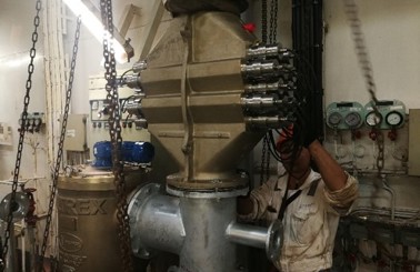 Worker inspecting large industrial valve system in a mechanical room.