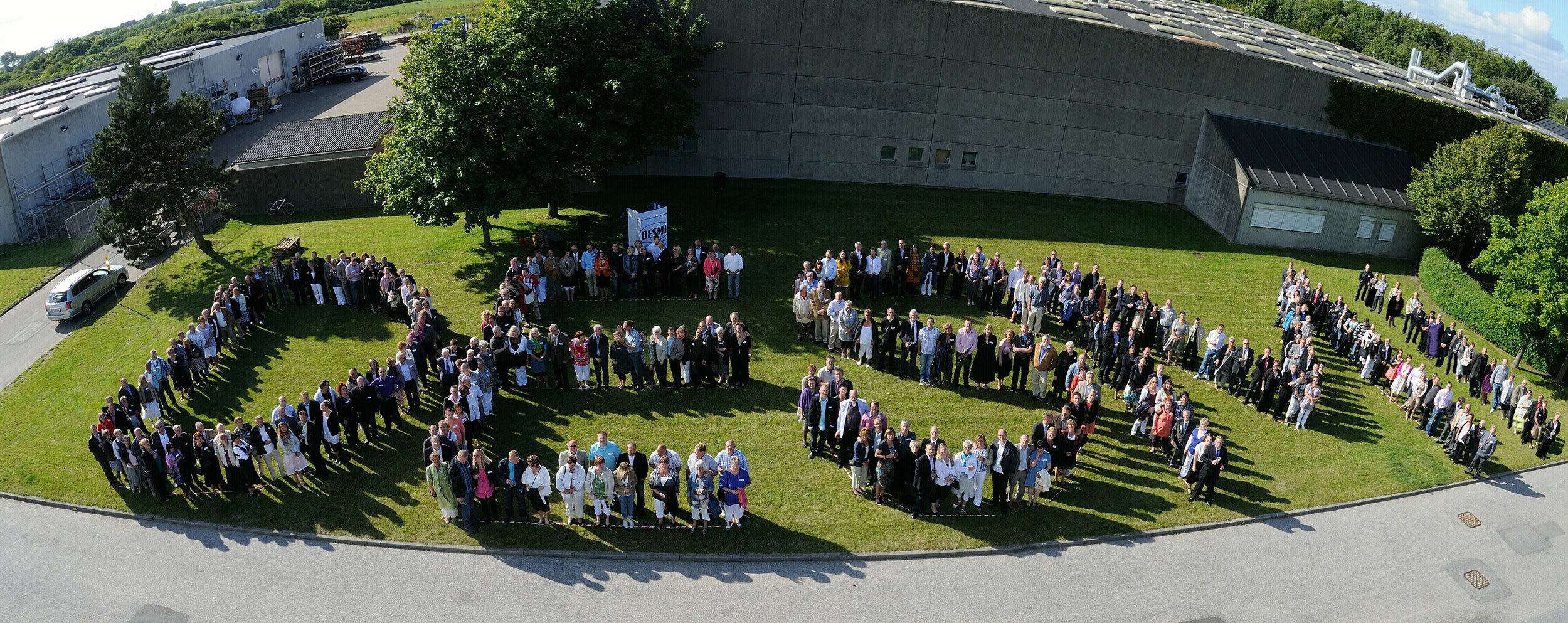 Aerial view of people forming the word "DESMI" on a grassy area.