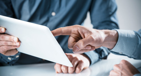 Two people discussing information on a tablet, one pointing at the screen.