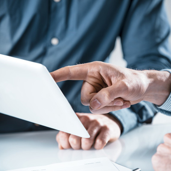 Two people discussing information on a tablet, one pointing at the screen.