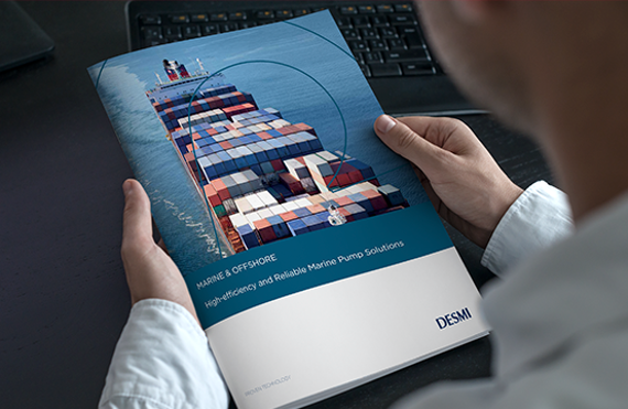 Person holding a DESMI brochure featuring a cargo ship and marine pump solutions.
