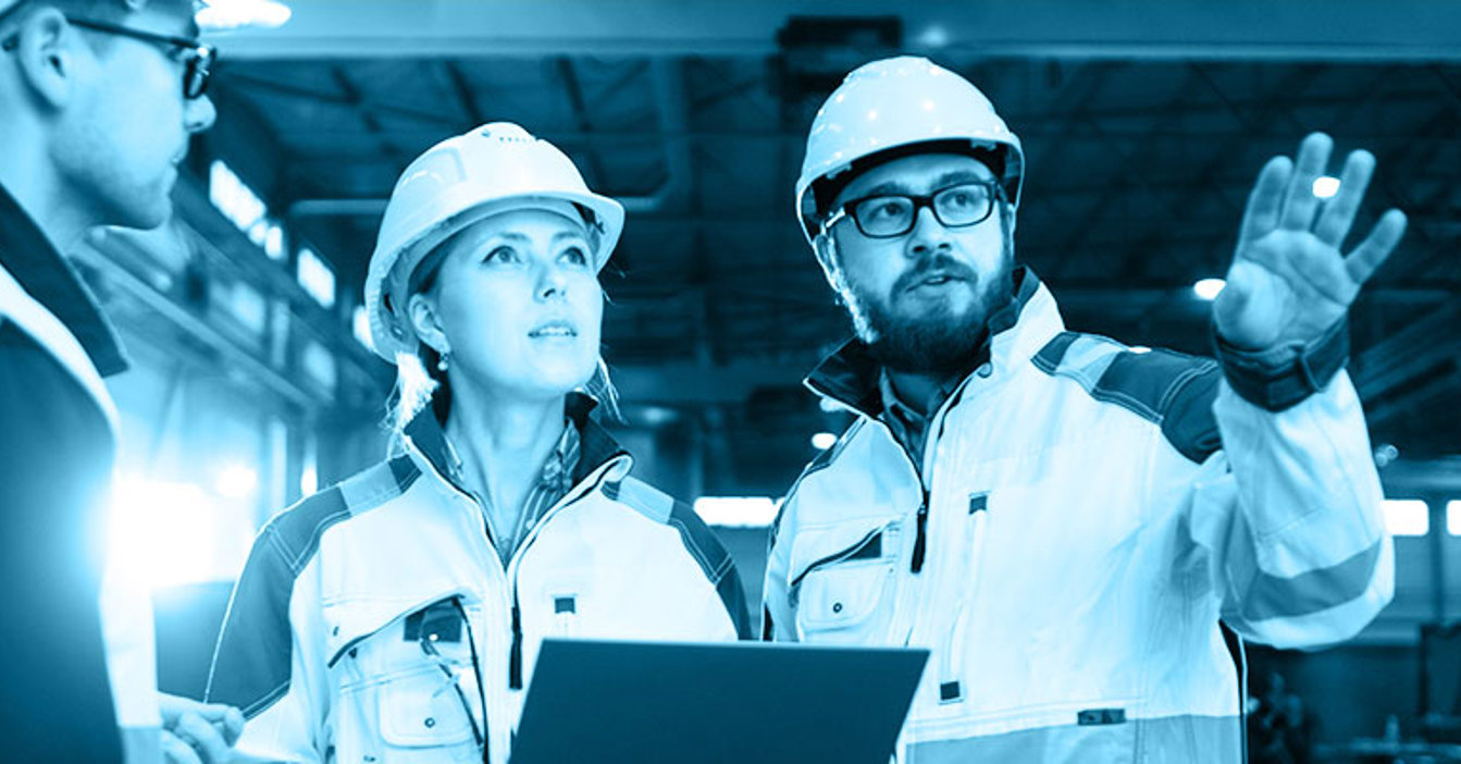 Engineers in hard hats discuss plans in an industrial facility.