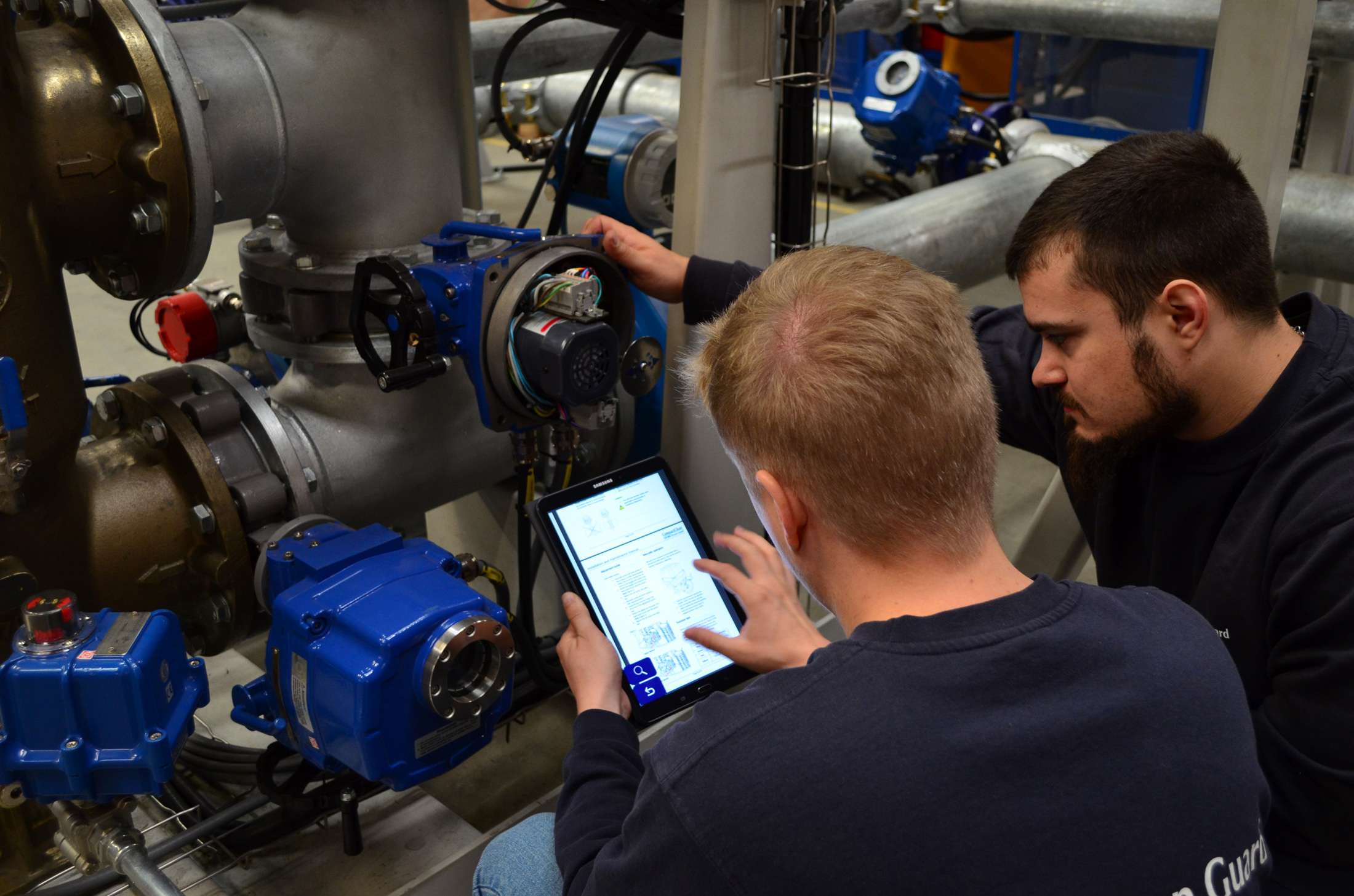Two technicians examine industrial equipment with a tablet for fluid handling maintenance.