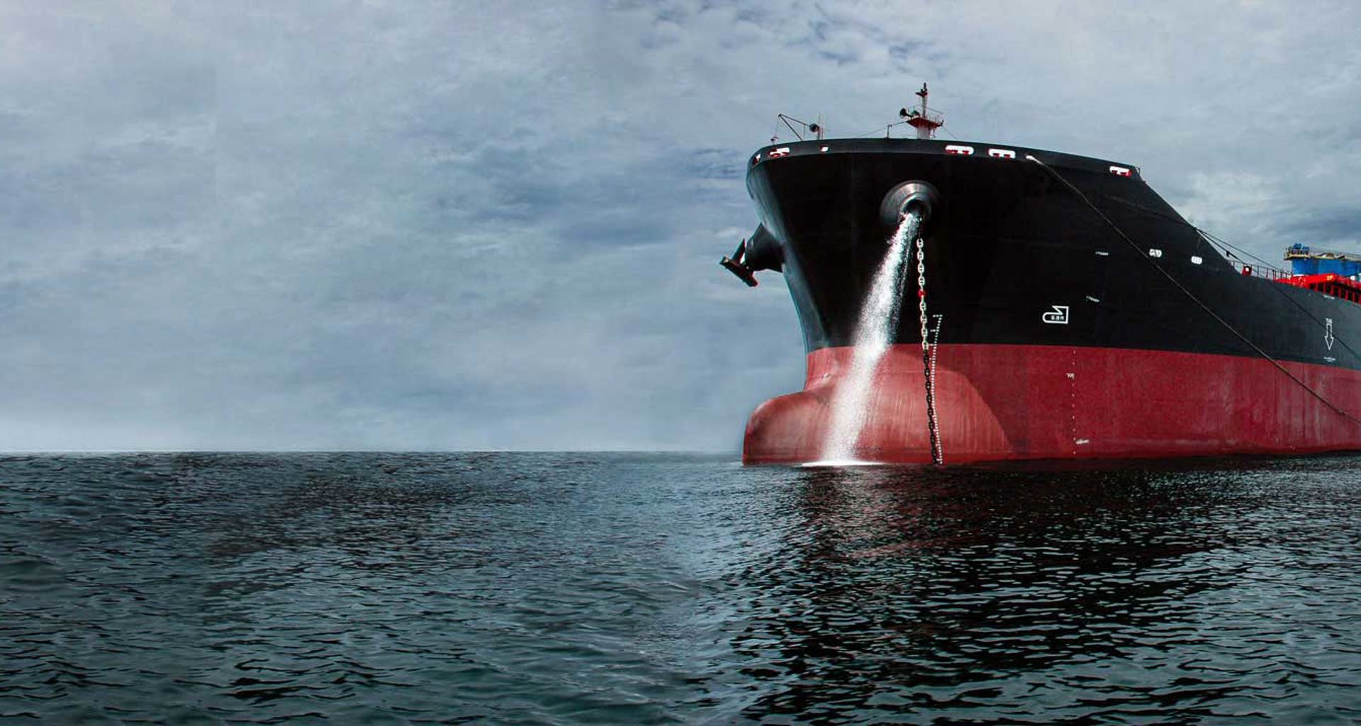 Large cargo ship releasing water into the ocean under cloudy skies.