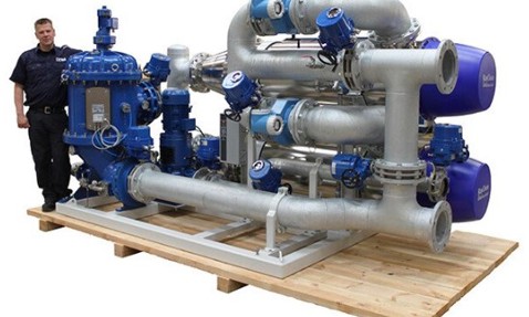 Industrial fluid handling system with multiple pumps and pipes, man standing beside.