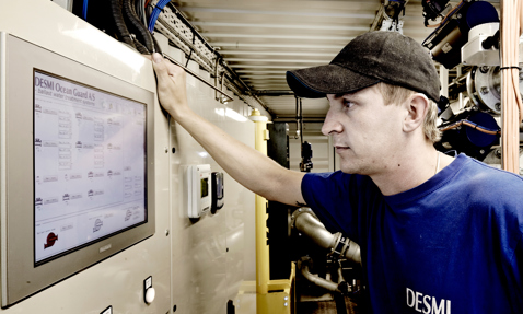 Technician operates DESMI Ocean Guard ballast water treatment system in industrial setting.