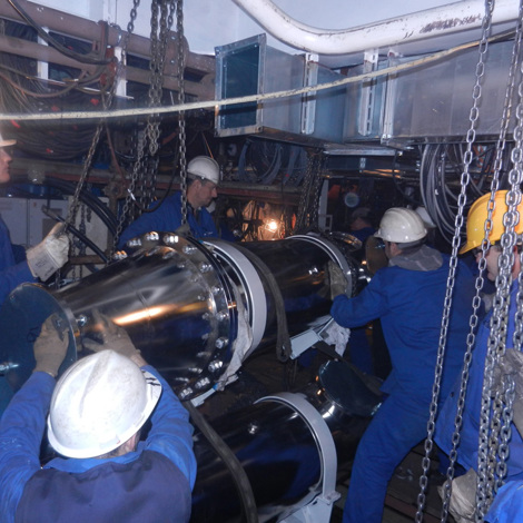 Workers installing large industrial equipment in a dimly lit mechanical room.