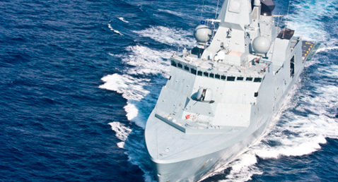 Naval warship sailing in open sea, creating waves in its wake.