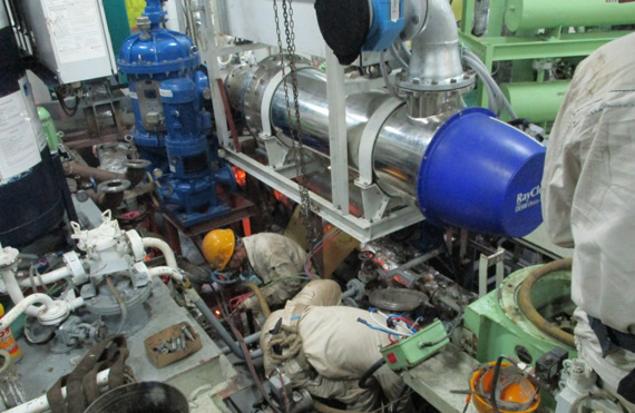 Workers installing machinery in an industrial setting with various pipes and equipment.