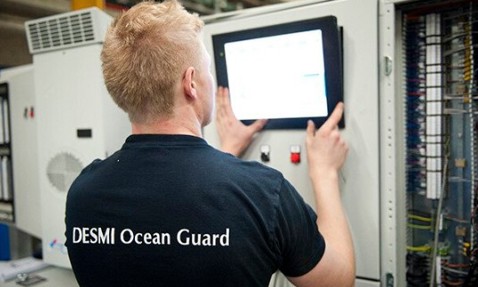 Person operating a control panel, wearing a "DESMI Ocean Guard" shirt.
