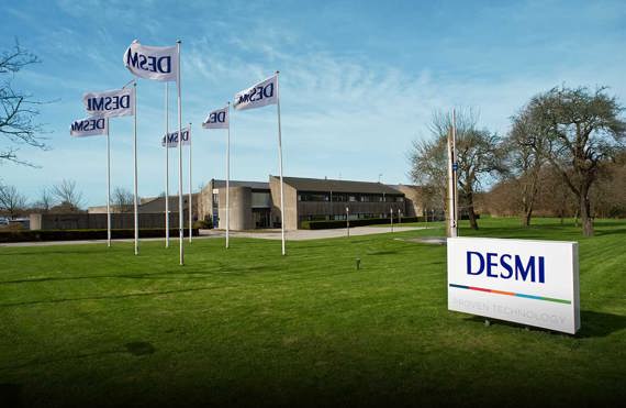 DESMI headquarters with flags and sign on a manicured lawn.