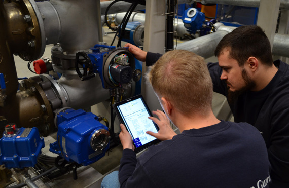 Two technicians inspecting industrial equipment, one using a tablet for reference.