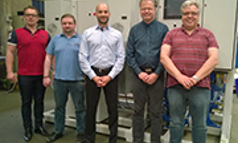 Five men standing in front of industrial equipment, posing for a group photo.