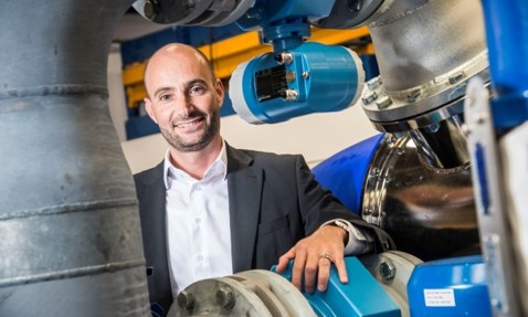 Man in suit standing beside industrial DESMI pumps and piping equipment.
