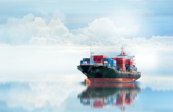 Cargo ship with colorful containers reflected on calm ocean water, under cloudy sky.