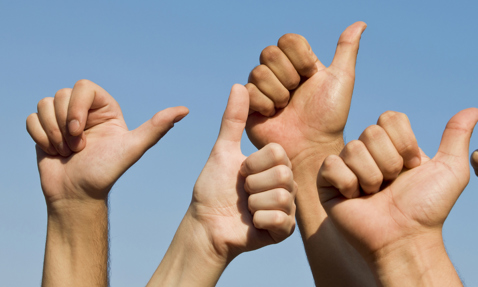 Several hands giving a thumbs-up against a clear blue sky.