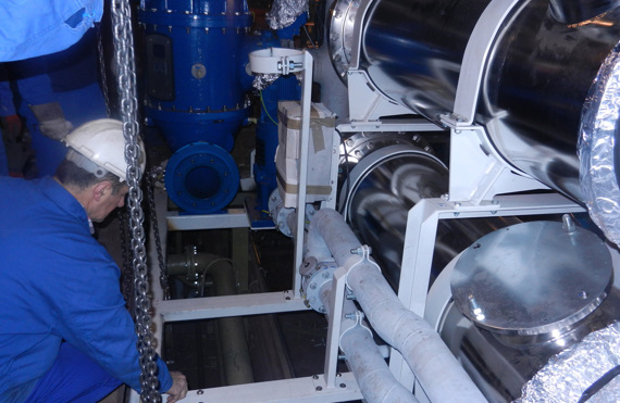 Technician working with industrial equipment and pipes in a mechanical room.