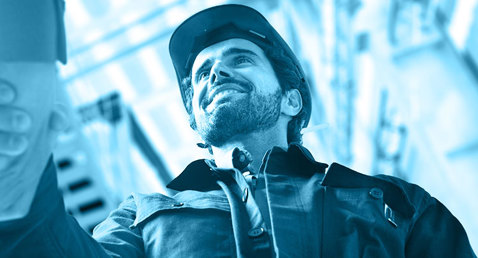 Worker in hard hat shaking hands, viewed from below, in industrial setting.