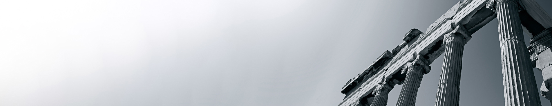 Ancient Greek columns against a clear, monochrome sky, viewed from below.