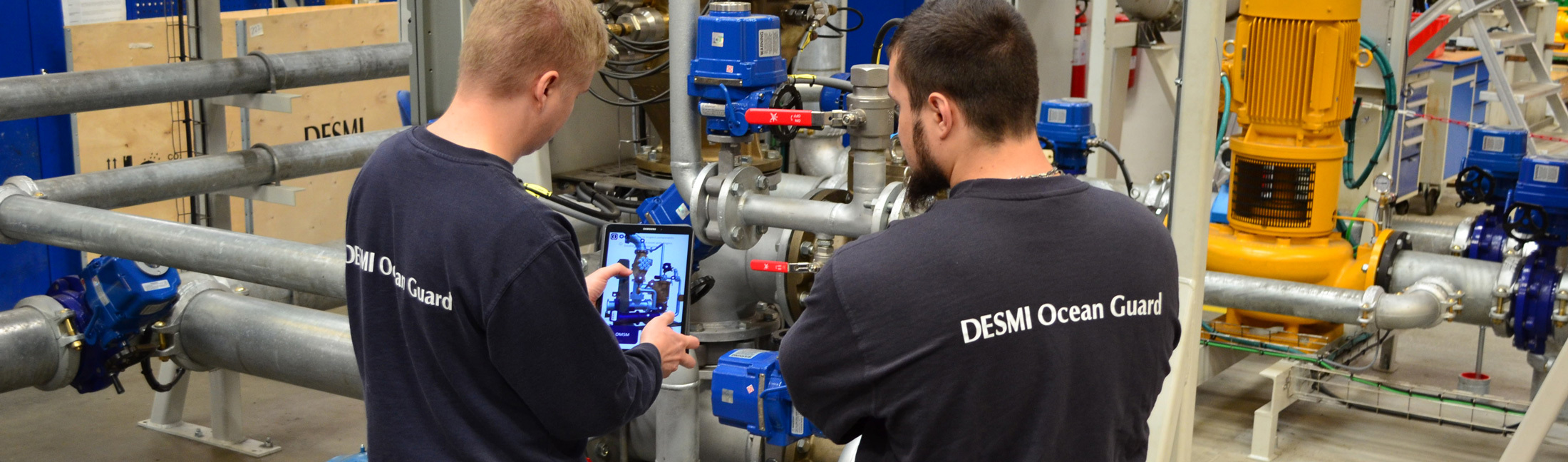 Two technicians inspect industrial equipment using a tablet at DESMI Ocean Guard facility.