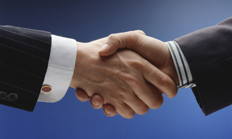 Two people in suits shaking hands against a blue background.