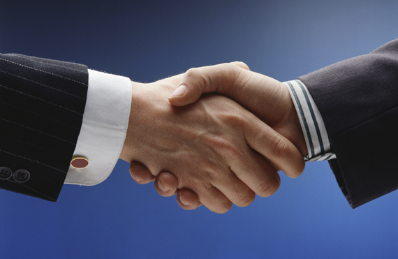 Two people in suits shaking hands against a blue background.