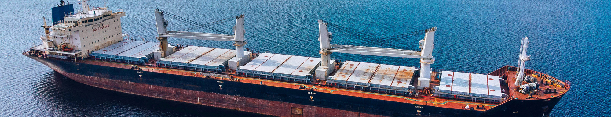 Cargo ship with cranes on a calm sea, labeled "No Smoking" on deck.