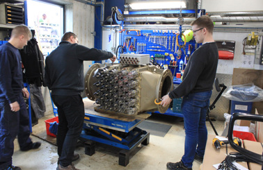 Three technicians work on large industrial equipment in a workshop.