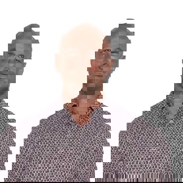 Bald man in a patterned shirt smiling at the camera against a white background.