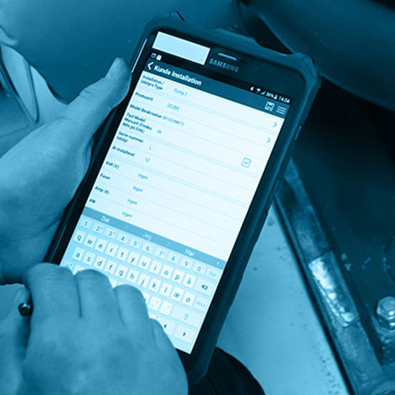 Person using a tablet near industrial equipment, possibly for data entry or diagnostics.