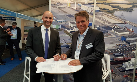 Two men signing documents at a booth with a port backdrop.