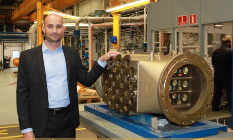 Man in a suit stands beside DESMI industrial equipment in a factory setting.