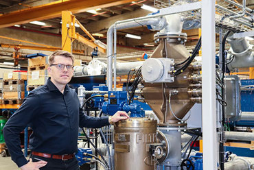 Man standing next to industrial equipment in a factory setting.