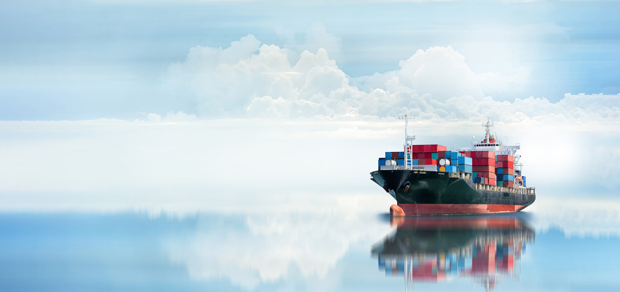 Cargo ship with colorful containers on calm water under cloudy sky.