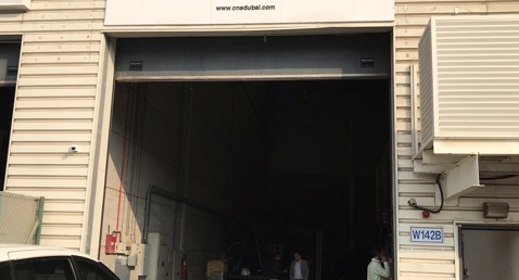 Warehouse entrance labeled "CNS Ships & Boats Repairing LLC" with vehicles parked outside.