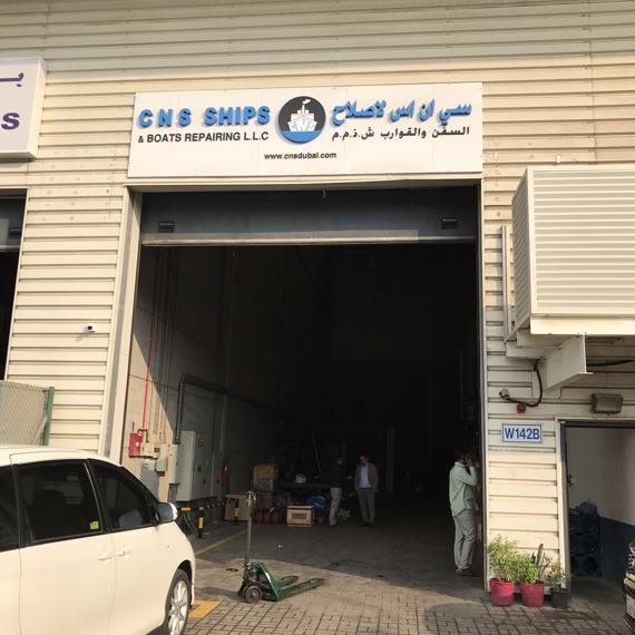 Warehouse entrance labeled "CNS Ships & Boats Repairing LLC" with vehicles parked outside.