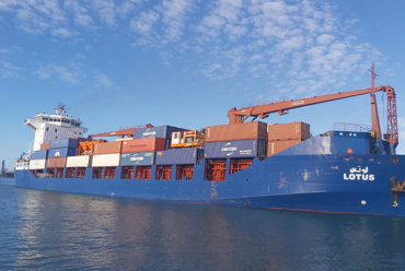 Blue cargo ship "Lotus" carrying stacked containers on a sunny day.