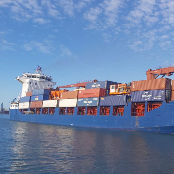 Blue cargo ship "Lotus" carrying stacked containers on a sunny day.