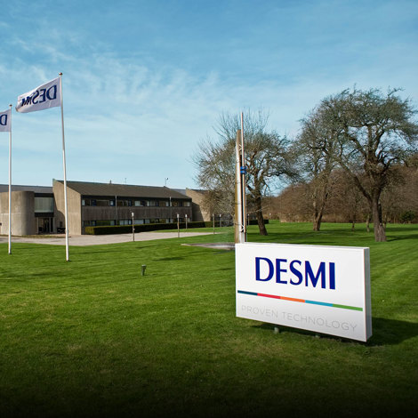 DESMI headquarters with flags and sign on a well-maintained lawn.
