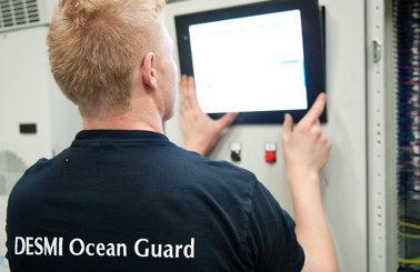 Technician operates control panel, wearing "DESMI Ocean Guard" shirt.